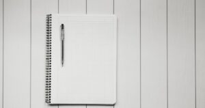 人物のいない白い方眼ノートとペンを背景に、飯田女子高校の2027年度入試と2コースを考えるイメージ