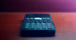人物のいない木製机に置かれた黒い電卓、岩国商業高校の2学科と2027年度入試を解説する横長サムネイル