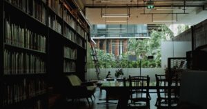 人物のいない明るい学校図書館の閲覧机と本棚を背景に、加治木高校の2027年度入試を考える写真