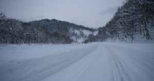 人物のいない雪原に一本の道が伸びる横長風景、横手高校の冬季通学と2027年度入試準備を考えるイメージ